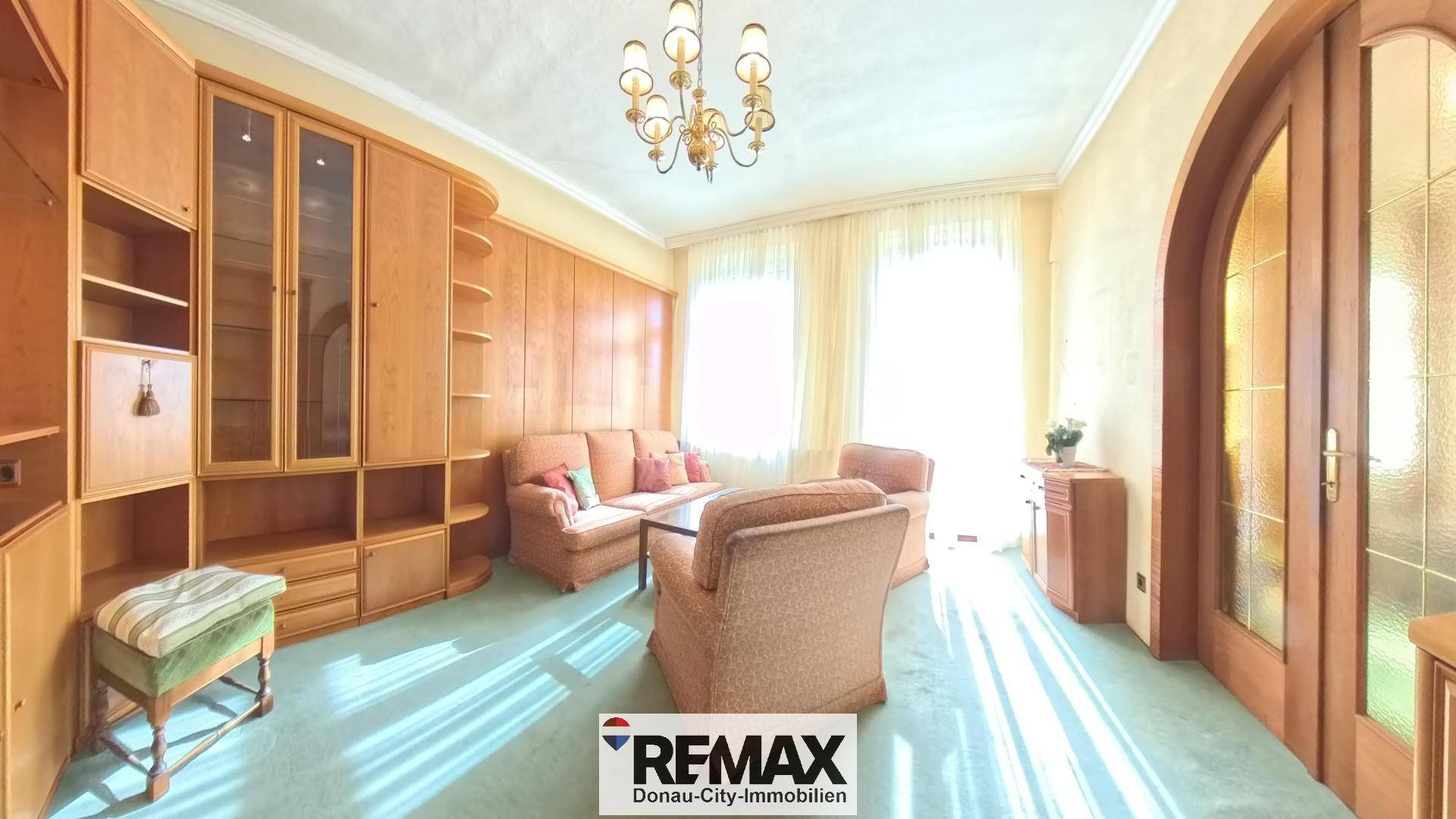 Gemütliches Wohnzimmer mit Teppichboden, Holzvertäfelung und klassischer Einrichtung, hell durch große Fenster.