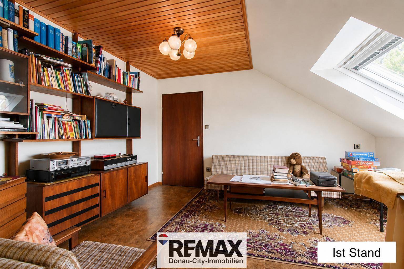 Dachgeschoss-Wohnraum mit Dachfenster, Bücherregalen und gemütlicher Sitzecke im Ist-Zustand.