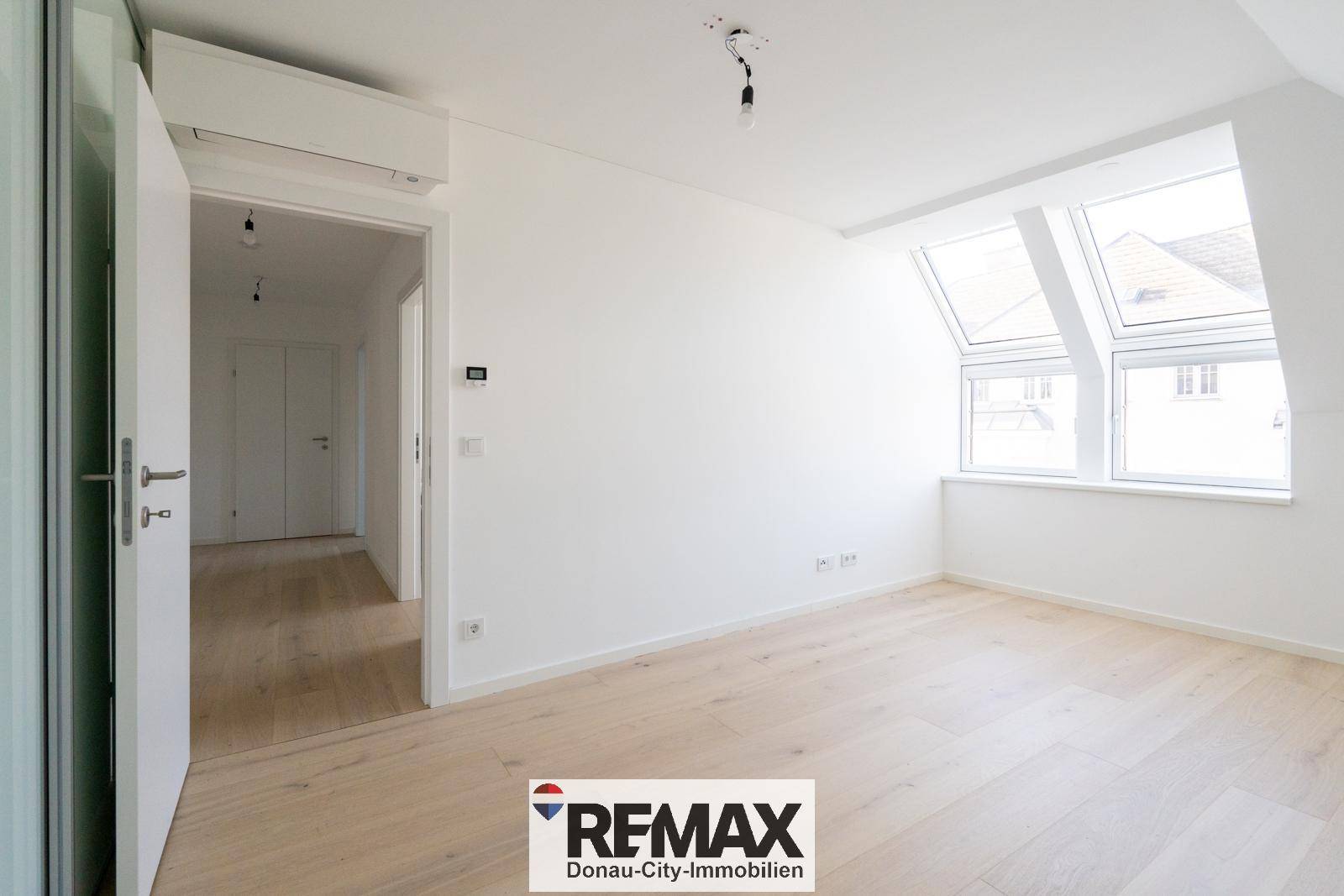 Helles Schlafzimmer mit Dachschrägen, Dachfenstern und Zugang zu einem weiteren Raum.