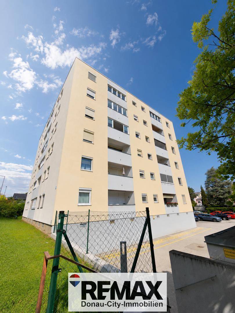 Mehrstöckiges Wohngebäude mit Balkonen und einer hellen Fassade unter blauem Himmel.