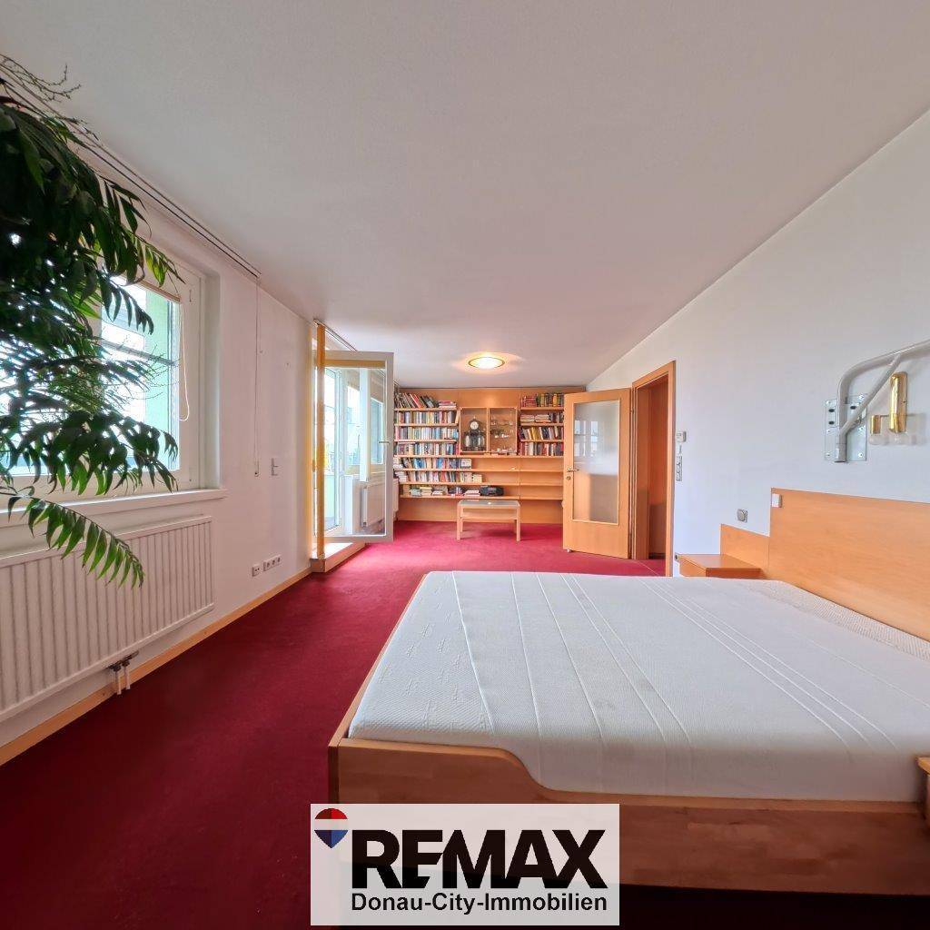 Helles Schlafzimmer mit rotem Teppichboden und Zugang zu einem Arbeitszimmer.