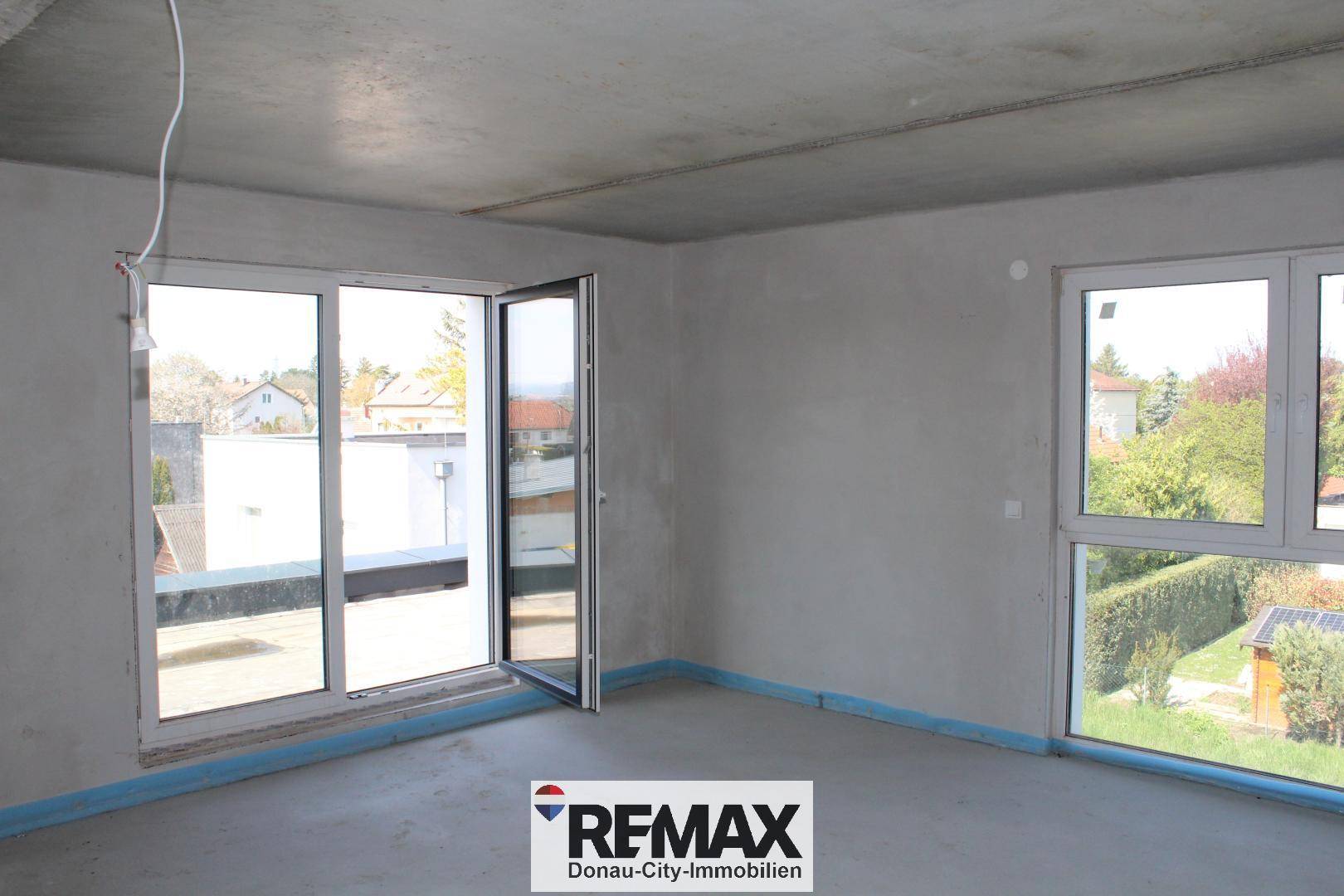 Unfertiger Raum mit großer Glastür, die zu einer potenziellen Dachterrasse führt, bietet viel Tageslicht.