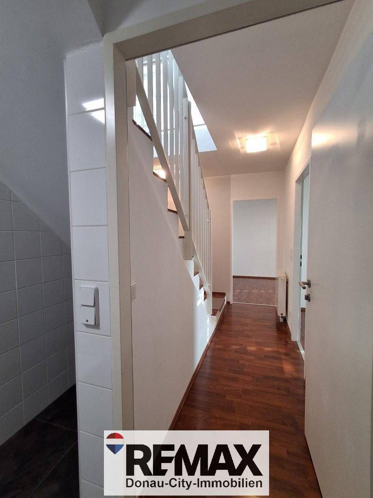 Heller Flur mit Holztreppe und dunklem Laminatboden, der die oberen Etagen verbindet.