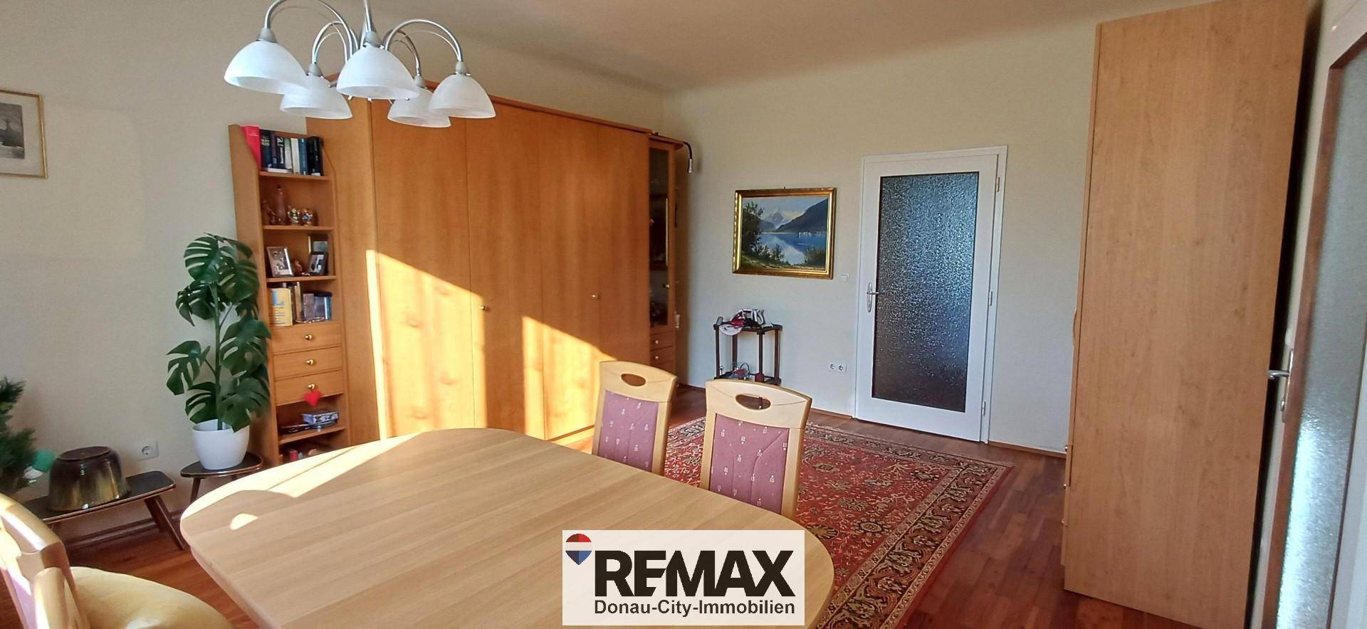 Heller Essbereich mit Holztisch, Stühlen und einem großen Holzschrank, durchflutet von Sonnenlicht.