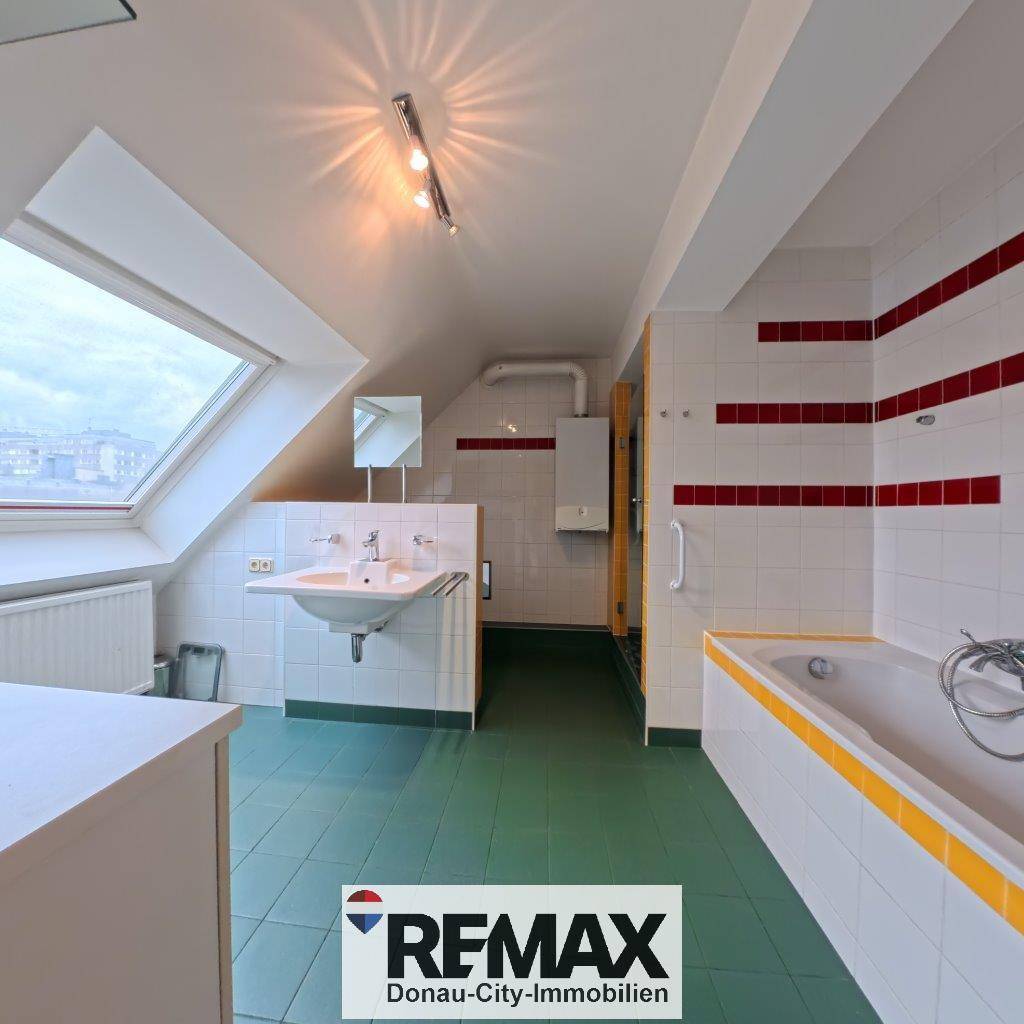 Geräumiges Badezimmer mit Dachfenster, Badewanne und farbigen Fliesen.