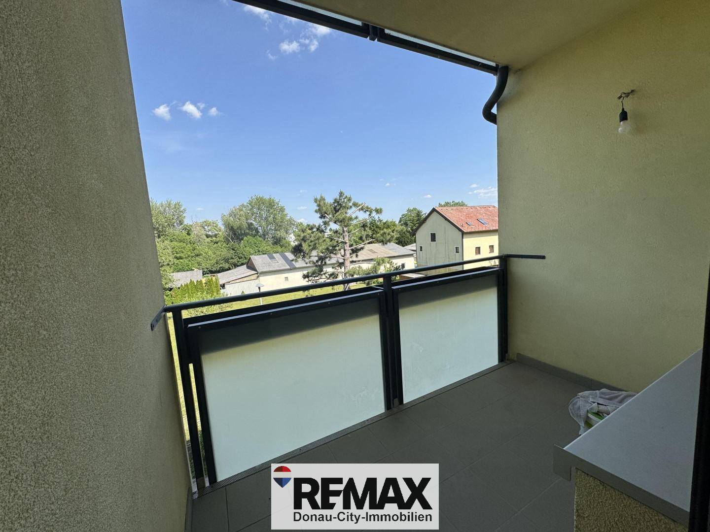Balkon mit Fliesenboden und Glasbrüstung, bietet einen grünen Ausblick auf die Umgebung.