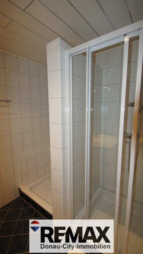 Duschkabine in einem Badezimmer mit weißen Wandfliesen und dunklem Boden.