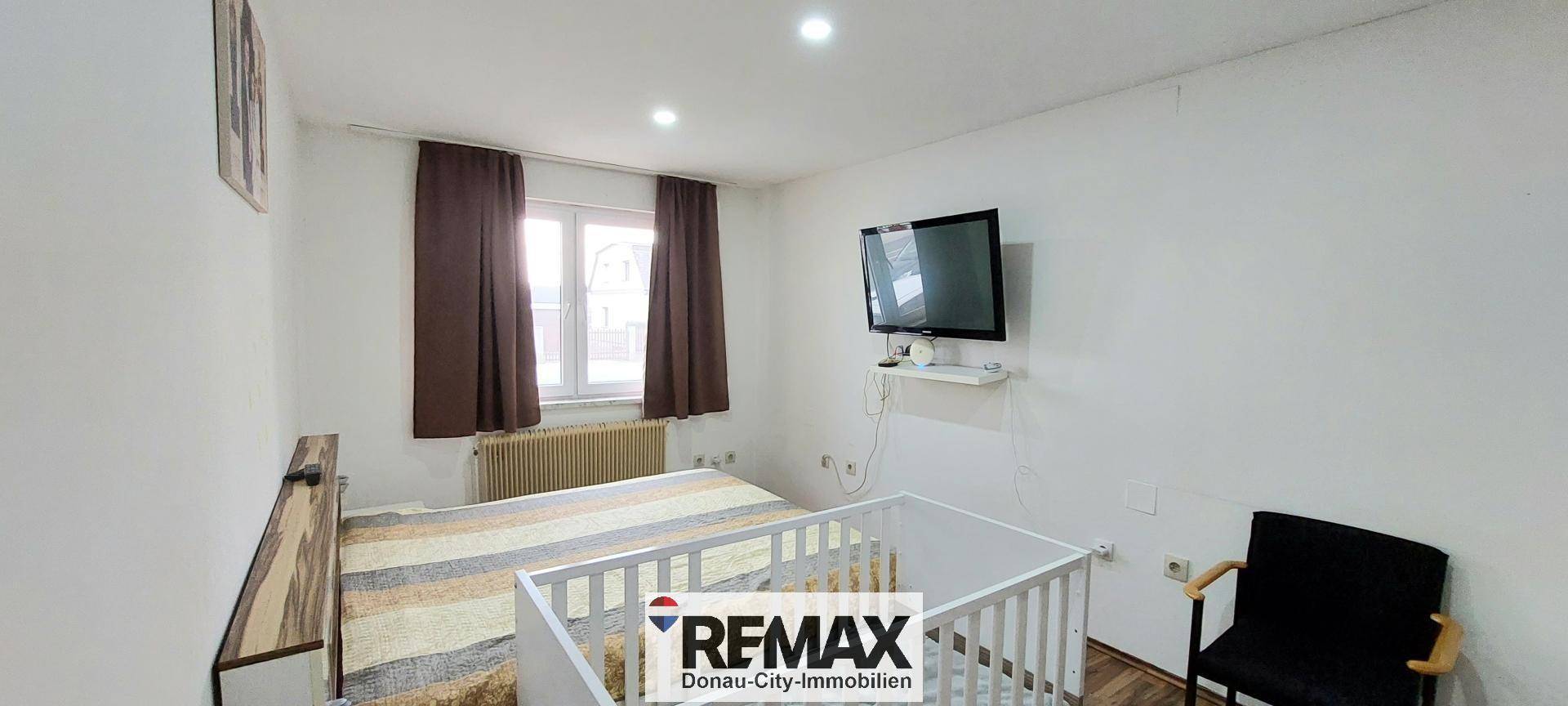 Schlafzimmer mit Doppelbett, Babybett und Fenster, hell und funktional eingerichtet.