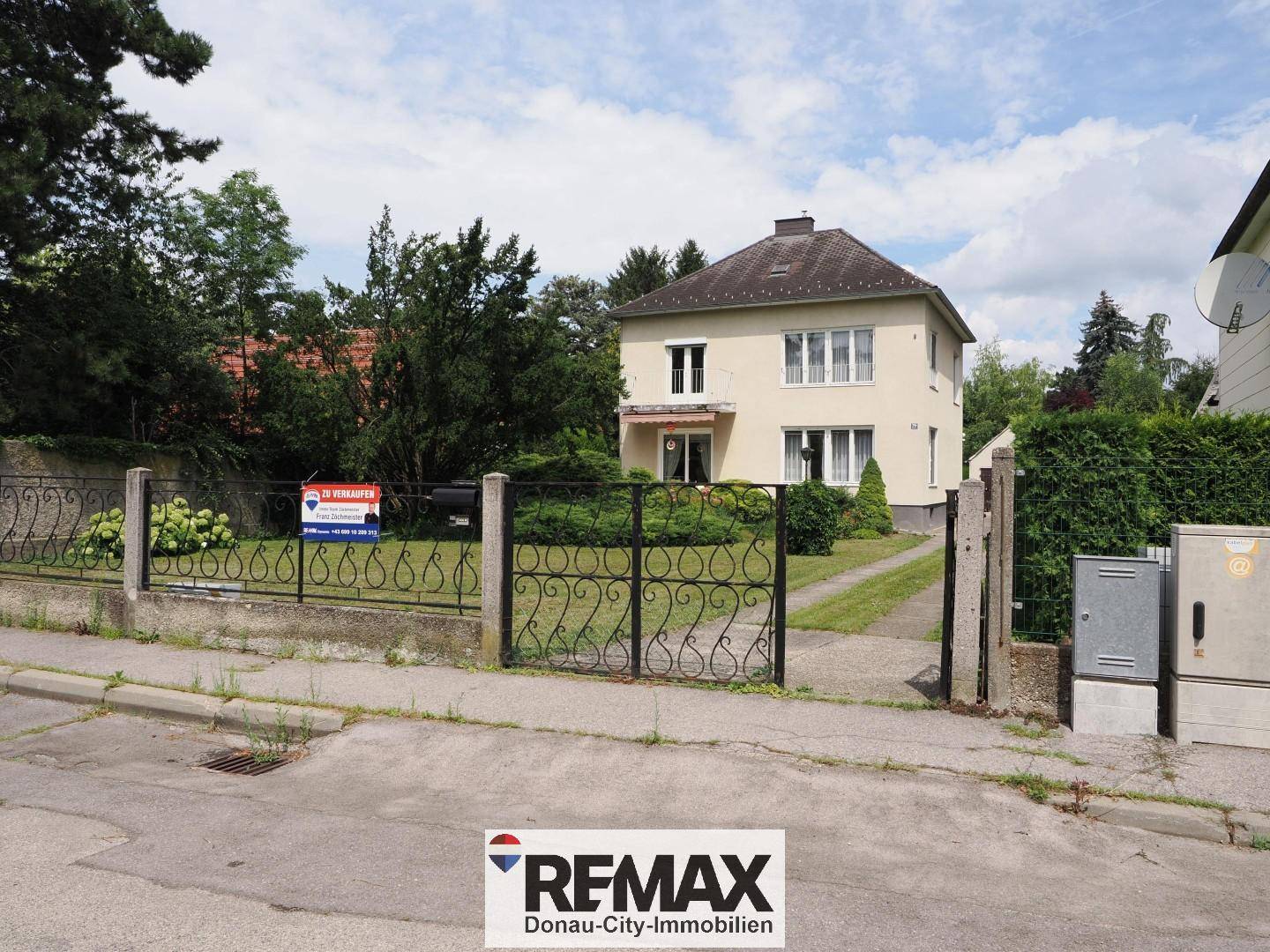 Einfamilienhaus von der Straße aus gesehen mit Zaun und 'Zu verkaufen'-Schild.