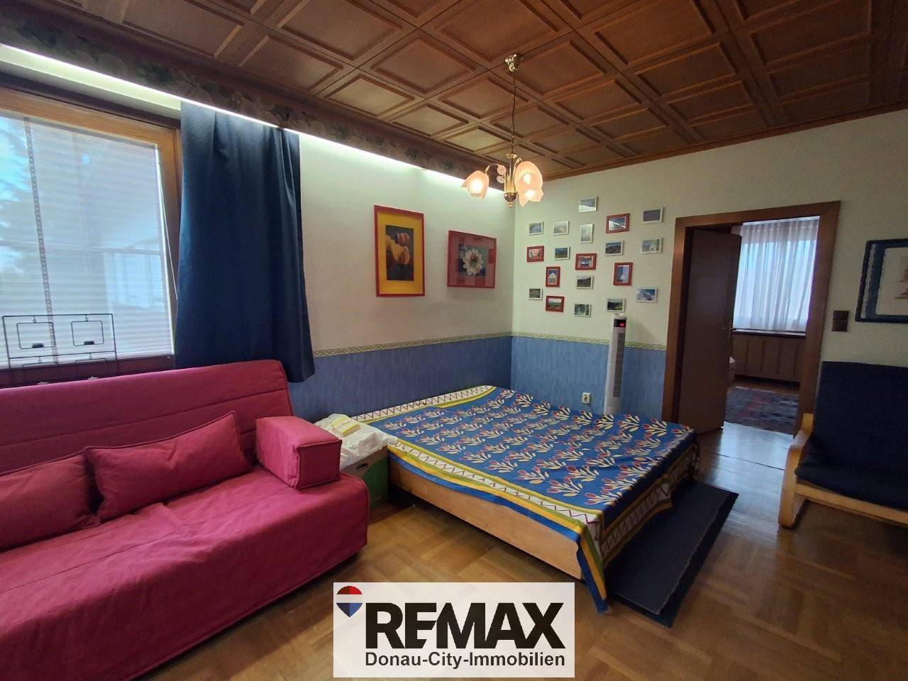 Gemütlicher Wohnraum mit Holzbalkendecke, rotem Sofa und Bett, dekoriert mit vielen Bildern.