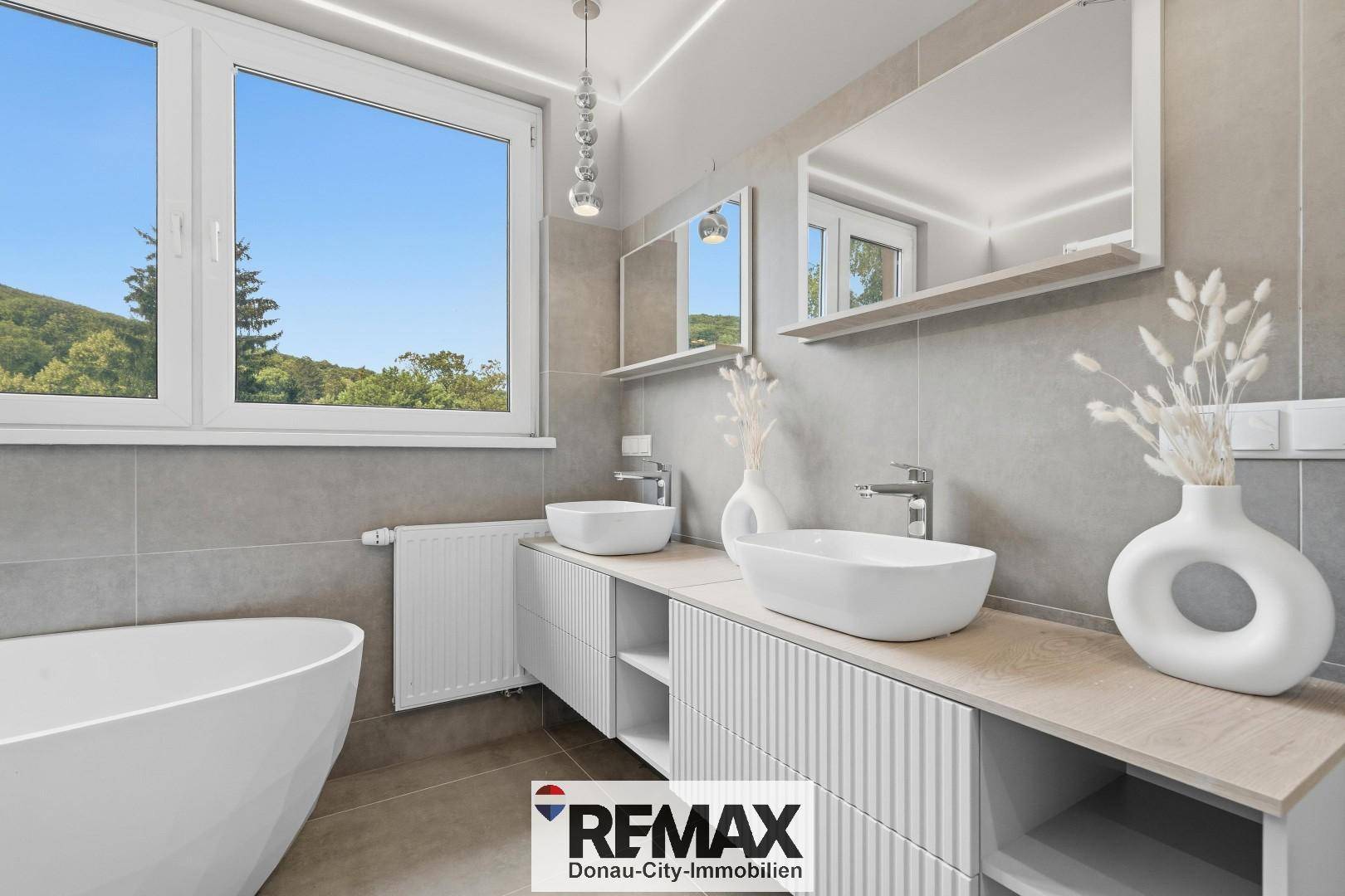 Elegantes Badezimmer mit zwei Aufsatzwaschbecken, freistehender Wanne und großem Fenster.