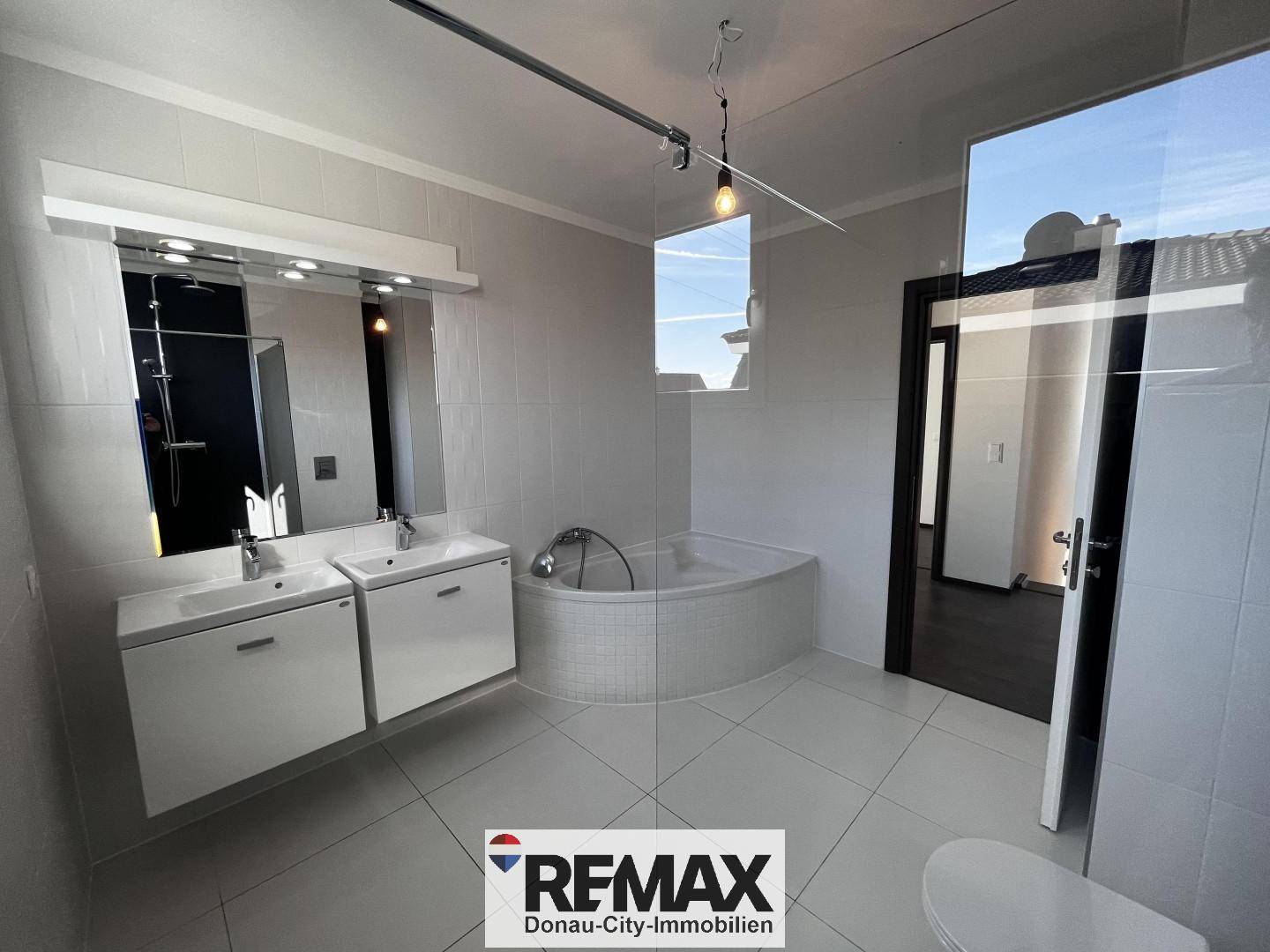 Modernes Badezimmer mit Doppelwaschbecken, Eckbadewanne und Dusche, hell gefliest.