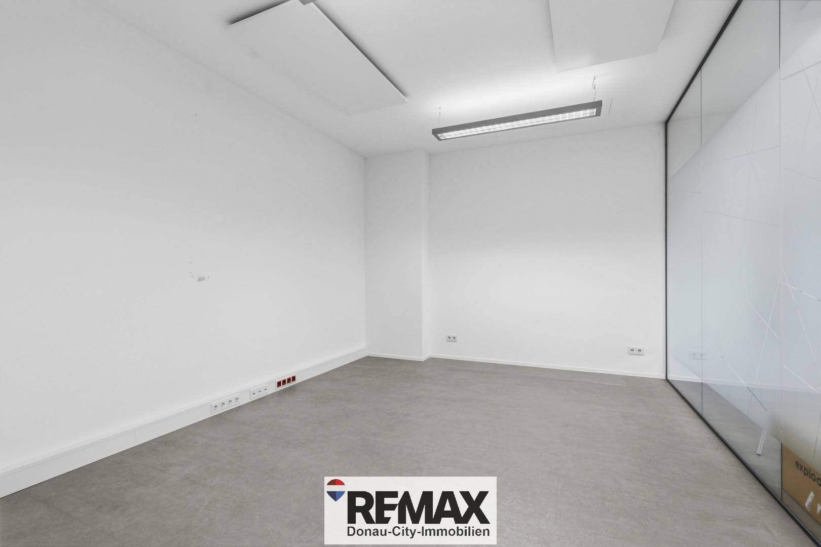 Leerer Büroraum mit weißen Wänden, Betonboden und Anschlussmöglichkeiten an der Wand.