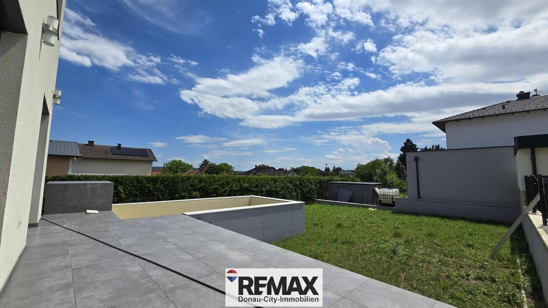 Große geflieste Terrasse mit Blick auf den grünen Rasen und den blauen Himmel.