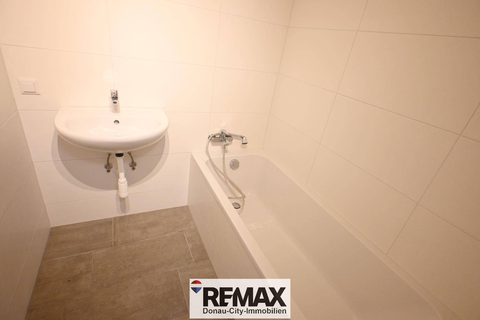 Einfaches Badezimmer mit Badewanne, Waschbecken und weißen Fliesen an den Wänden.
