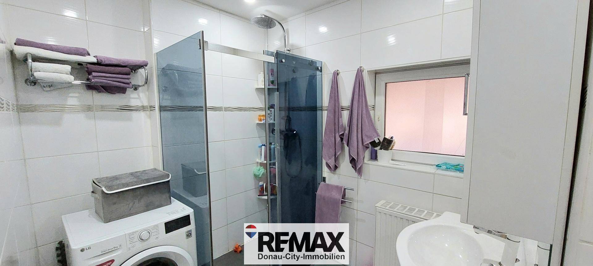 Helles Badezimmer mit Dusche, Waschbecken und Waschmaschine, praktisch und modern.