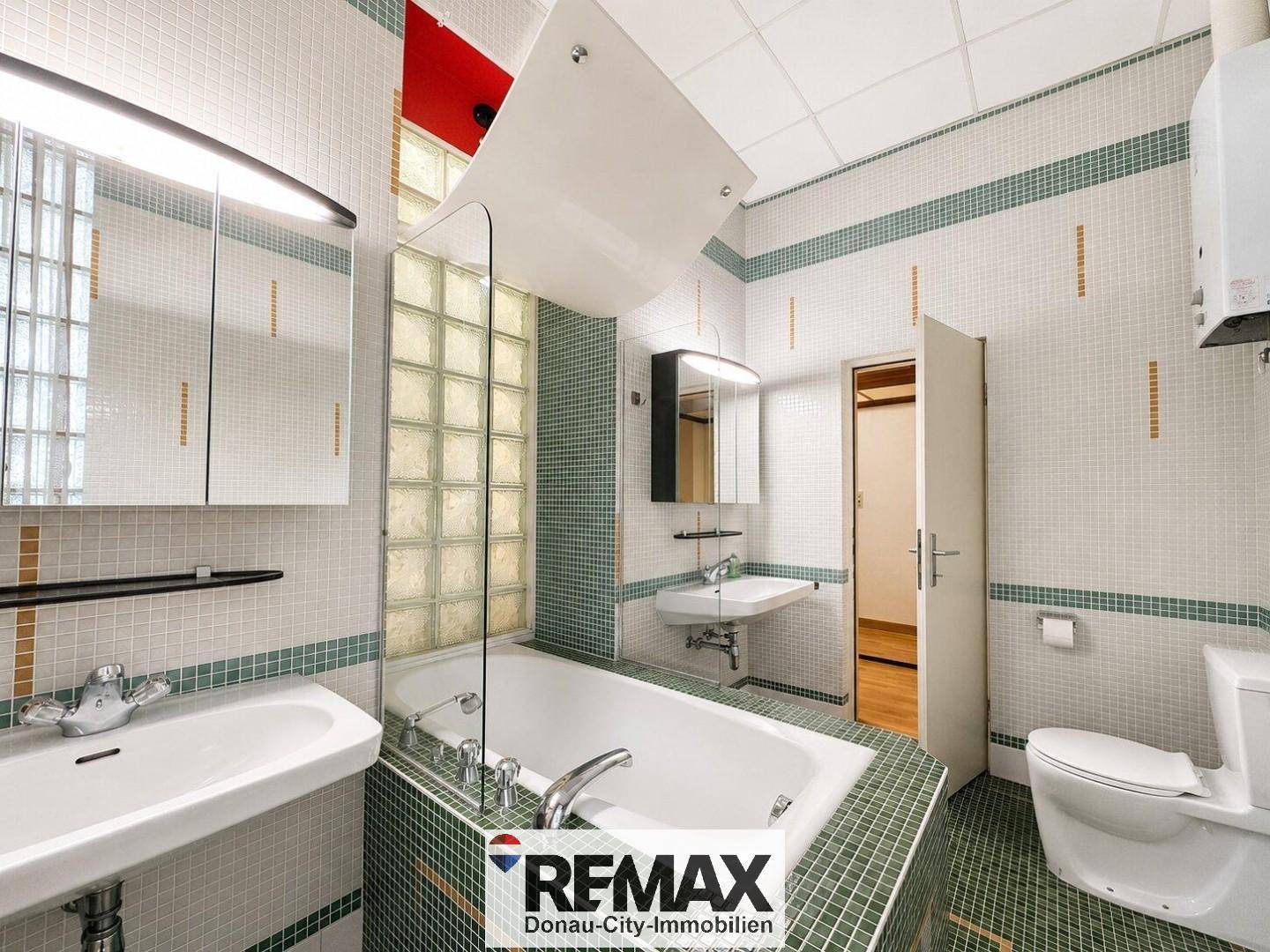 Funktionales Badezimmer mit Toilette, Waschbecken und Spiegelschrank, in grünen und weißen Fliesen.