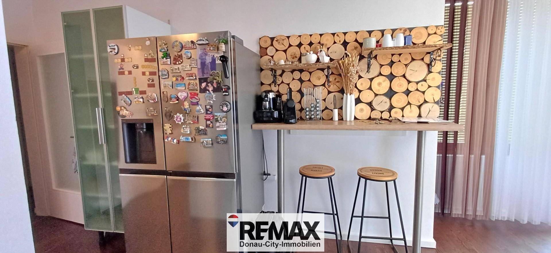 Funktionale Küche mit großem Kühlschrank, Frühstücksbar und dekorativer Holzwand.