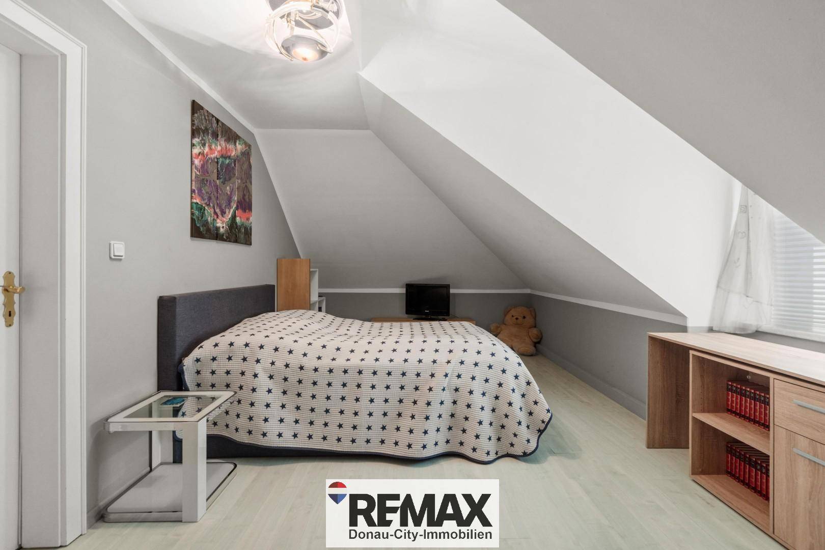 Gemütliches Schlafzimmer im Dachgeschoss mit Dachschrägen, hellem Boden und einem bequemen Bett.