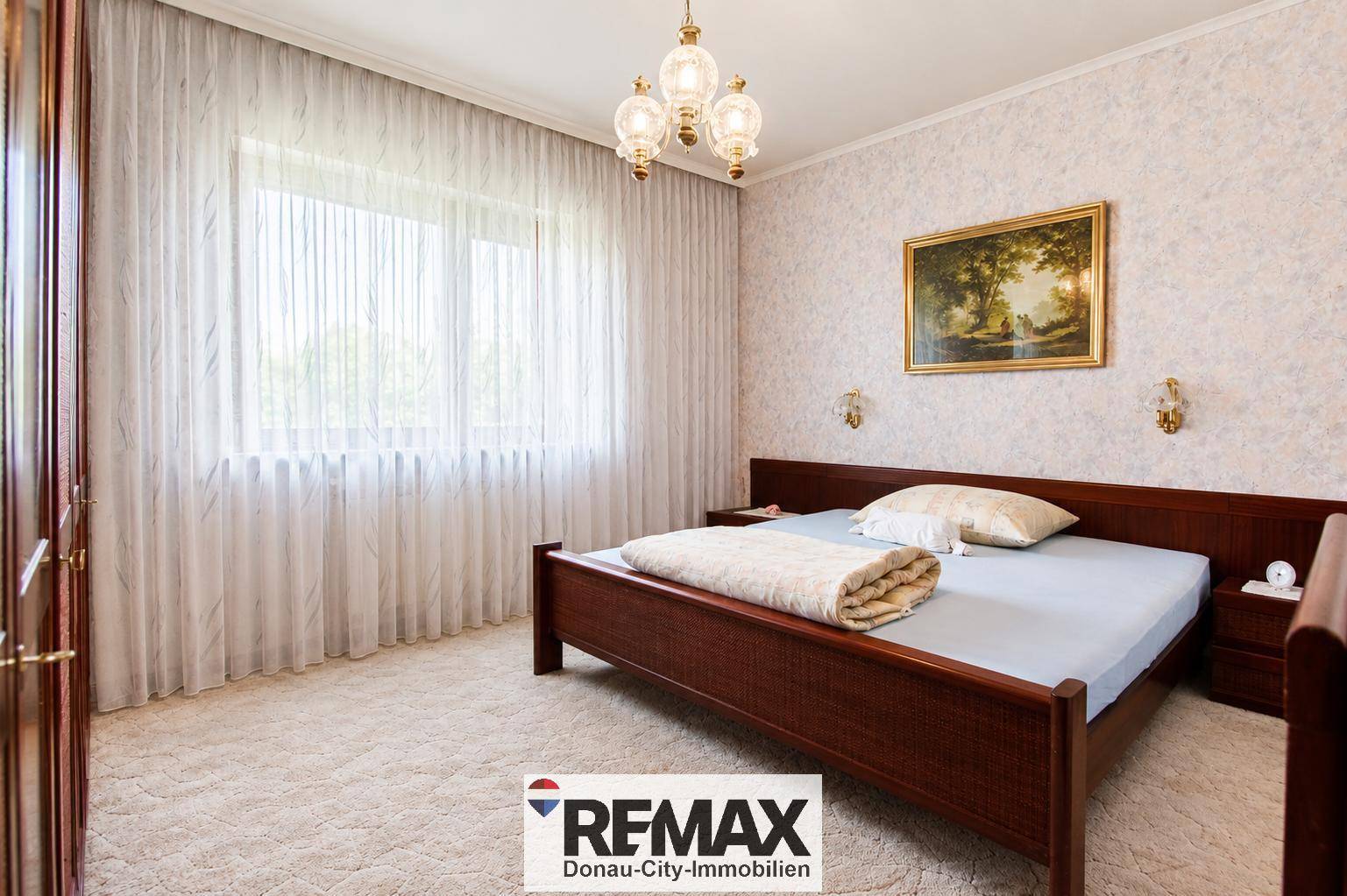 Helles Schlafzimmer mit großem Fenster, Teppichboden und klassischem Holzbett, bietet viel Tageslicht.