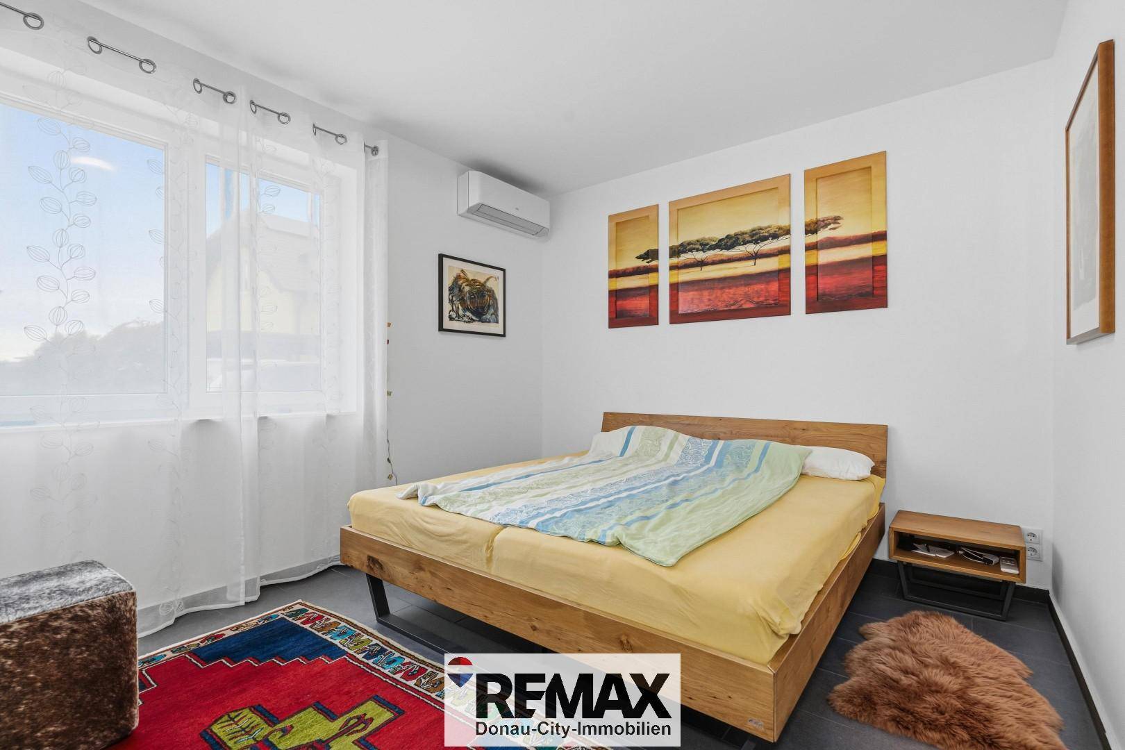 Schlafzimmer mit Holzbett, Teppich und Klimaanlage, hell und gemütlich eingerichtet.