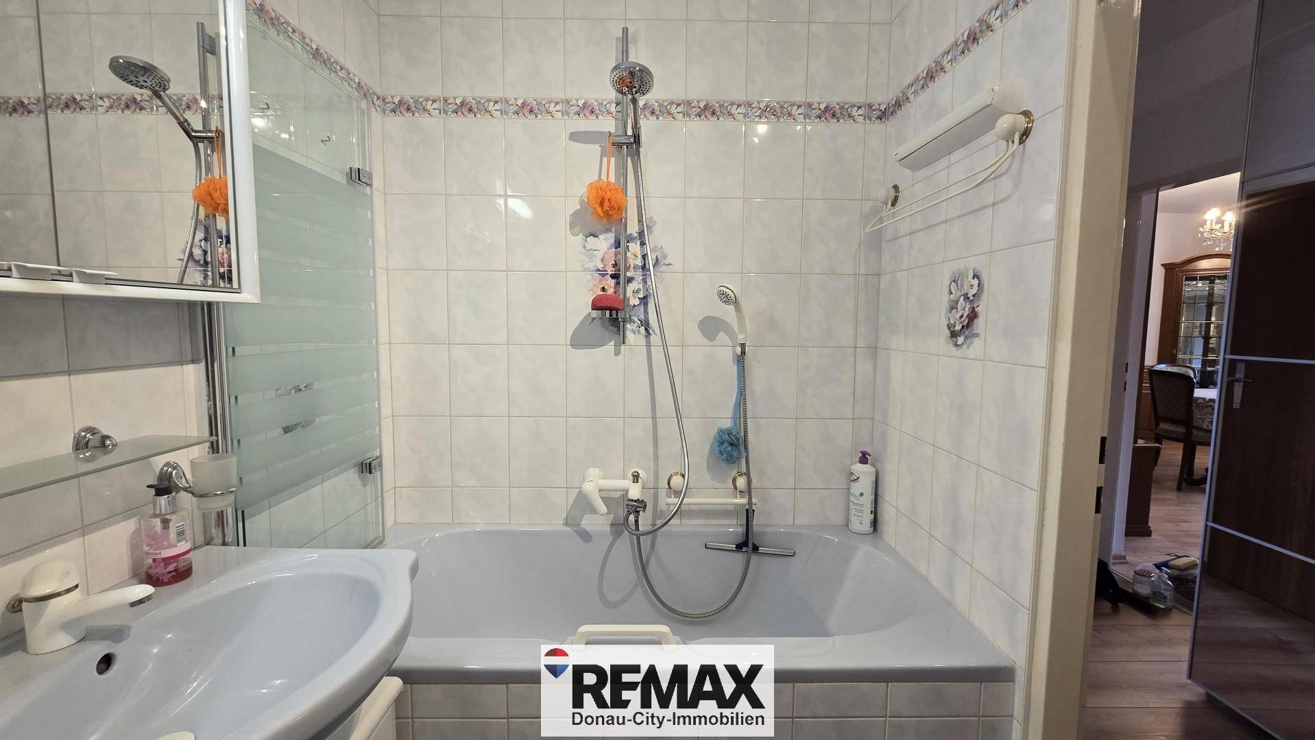 Badezimmer mit Badewanne und Duschvorrichtung, hell gefliest und funktional ausgestattet.