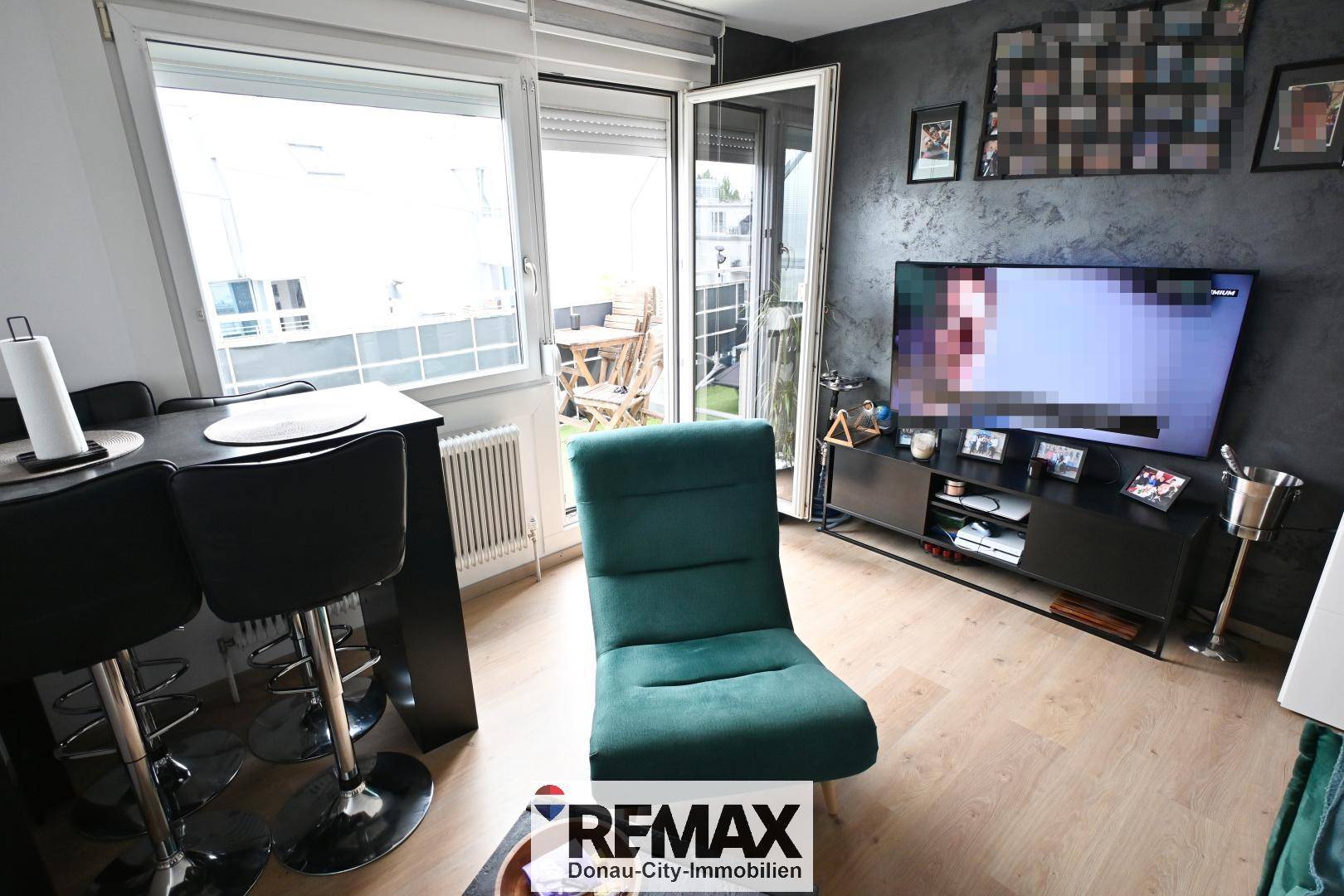 Wohnbereich mit großem Fernseher, dunkler Akzentwand und direktem Zugang zum möblierten Balkon.
