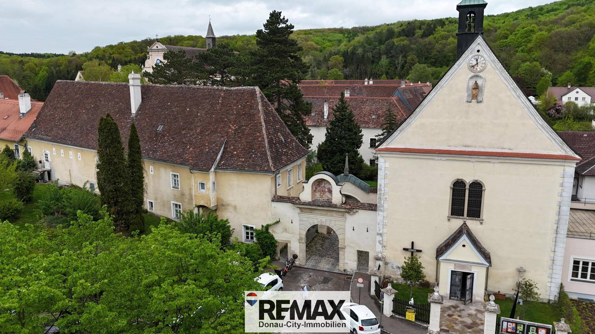 Historischer Gebäudekomplex mit Kirche und Torbogen, umgeben von viel Grün.