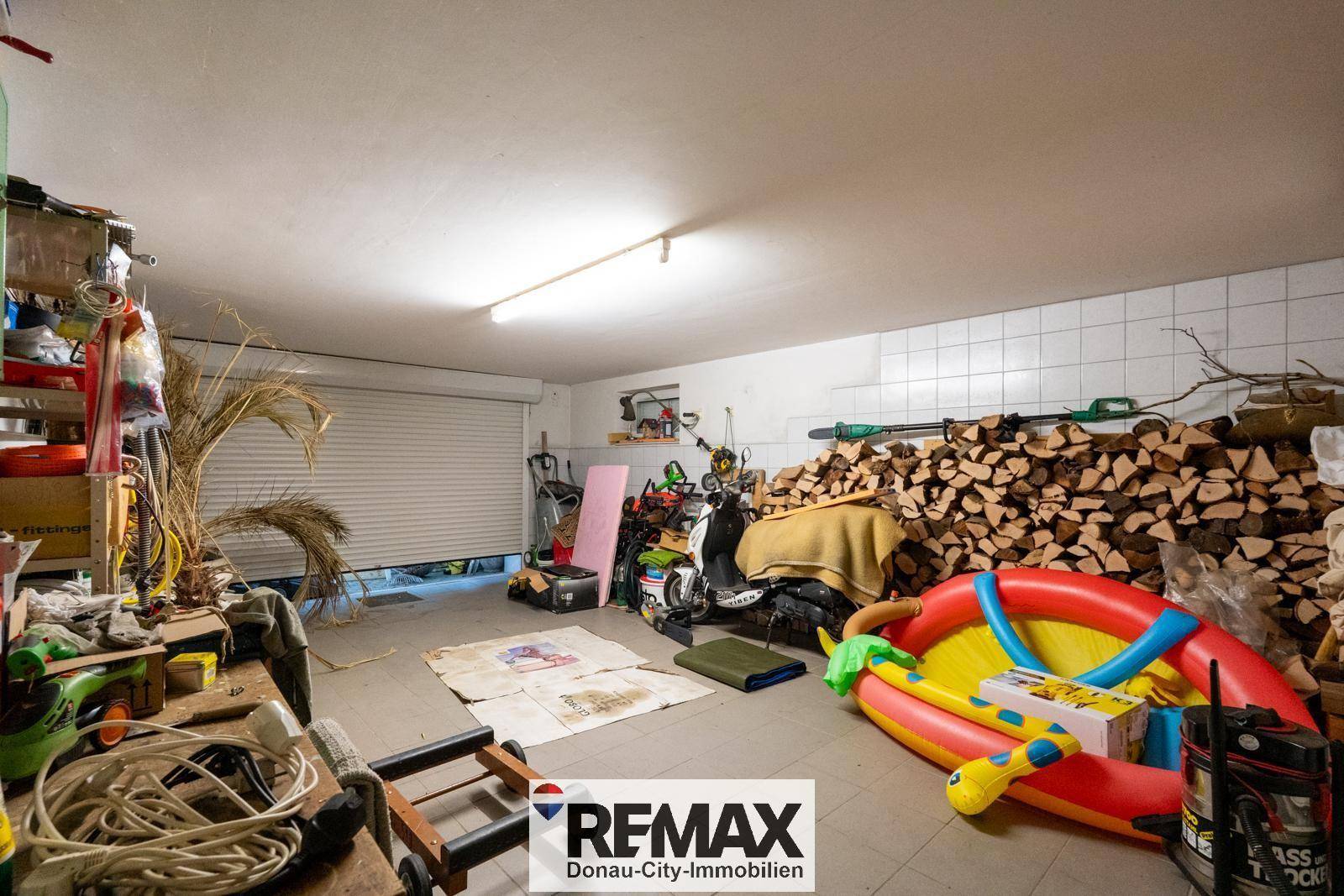 Geräumige Garage mit Rolltor, genutzt als Lagerraum für Brennholz und diverse Gegenstände.