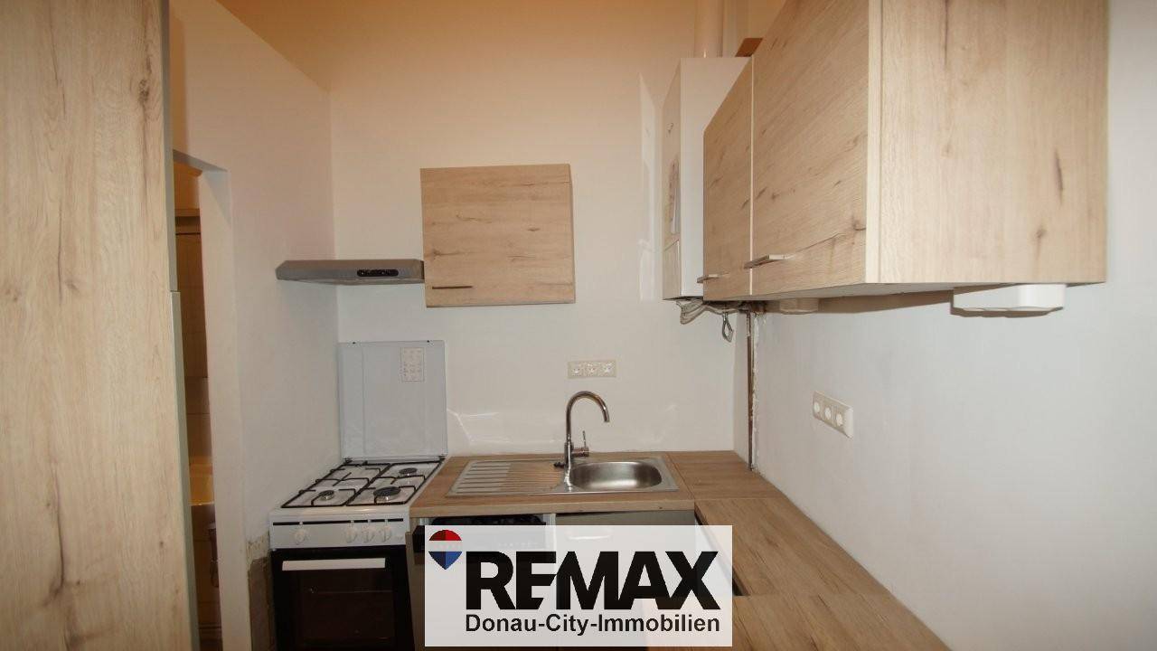 Kleine Küche mit Holzoptik-Schränken, Gasherd und Dunstabzugshaube, funktional eingerichtet.