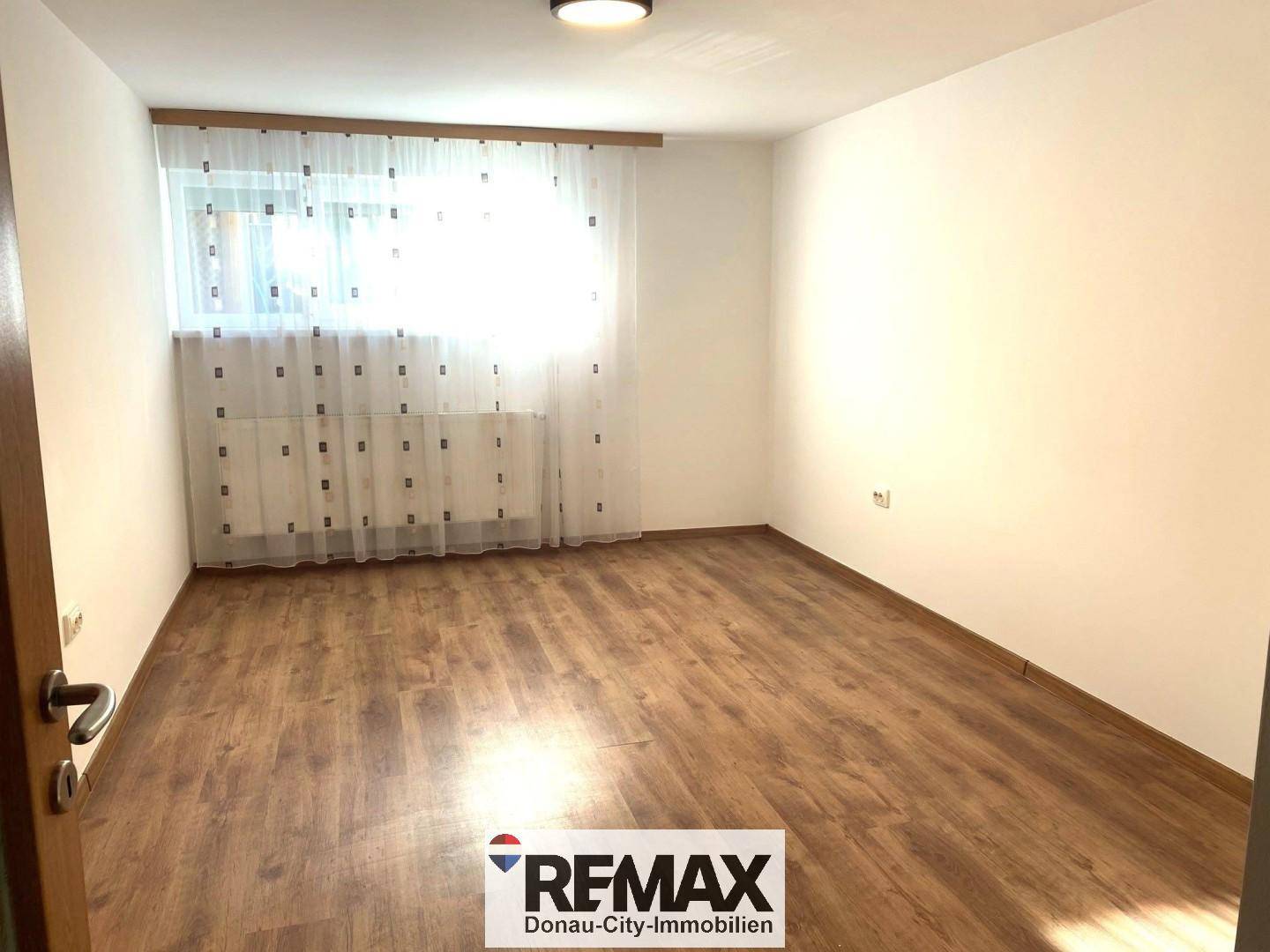 Heller, leerer Raum mit Laminatboden und großem Fenster, bereit zur individuellen Gestaltung.