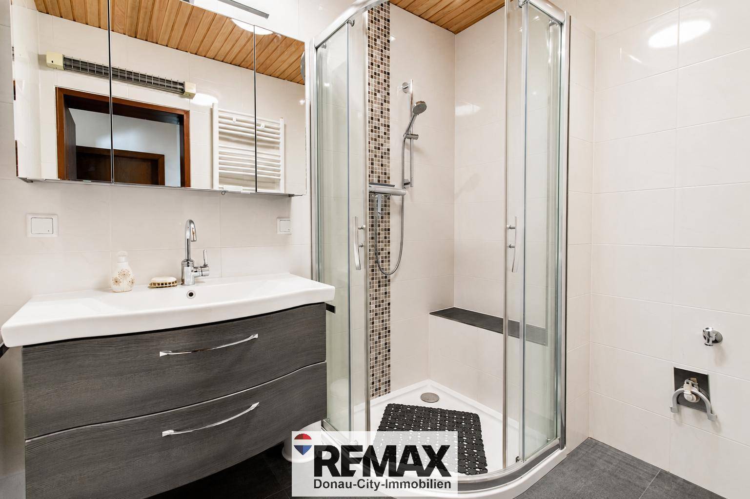Modernes Badezimmer mit Duschkabine, Waschtisch und Holzdecke, funktional und hell gestaltet.