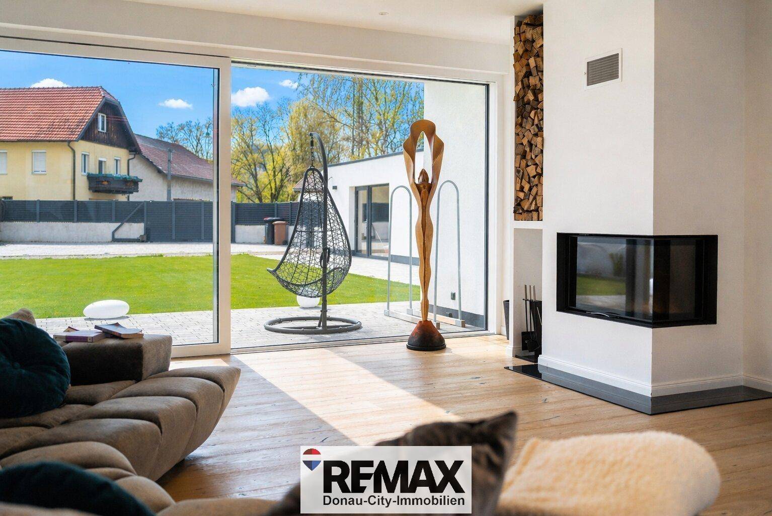 Helles Wohnzimmer mit Kamin, Holzboden und großen Fenstern zum grünen Garten.
