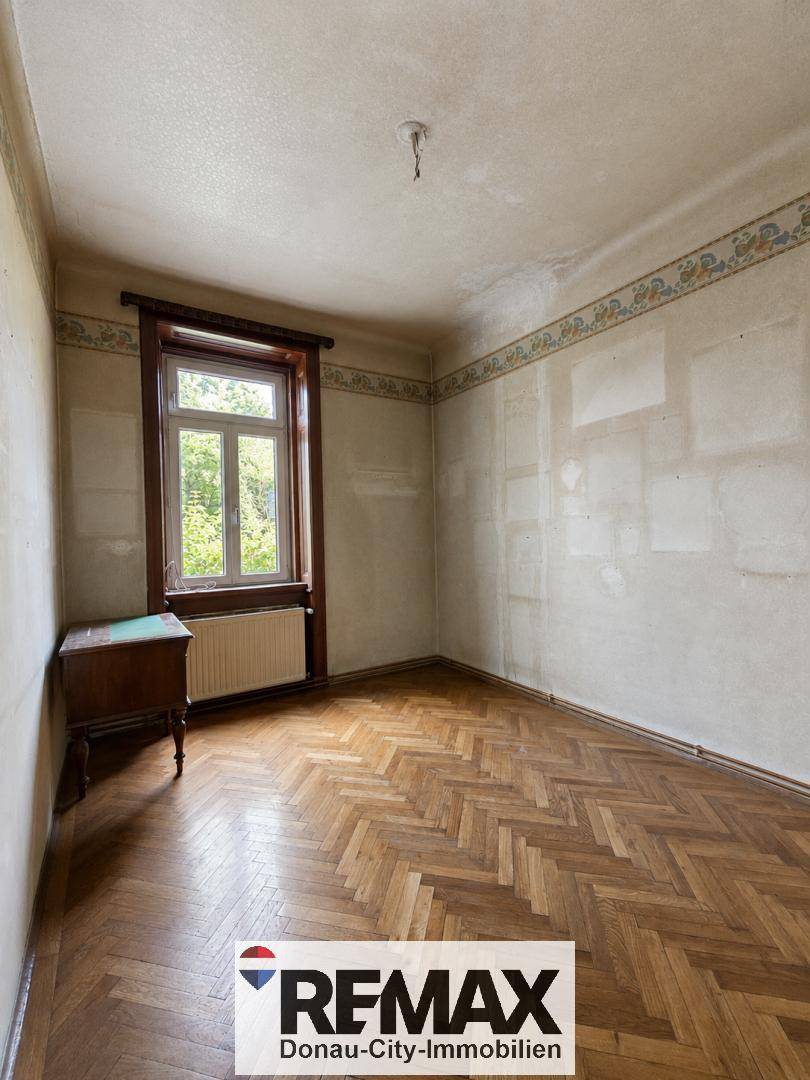 Leeres Schlafzimmer mit Fischgrätparkett und Wänden, die auf eine Renovierung warten.