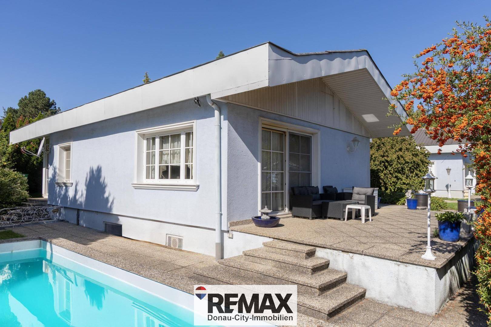 Außenansicht des Hauses mit einer Terrasse und einem erfrischenden Swimmingpool unter blauem Himmel.