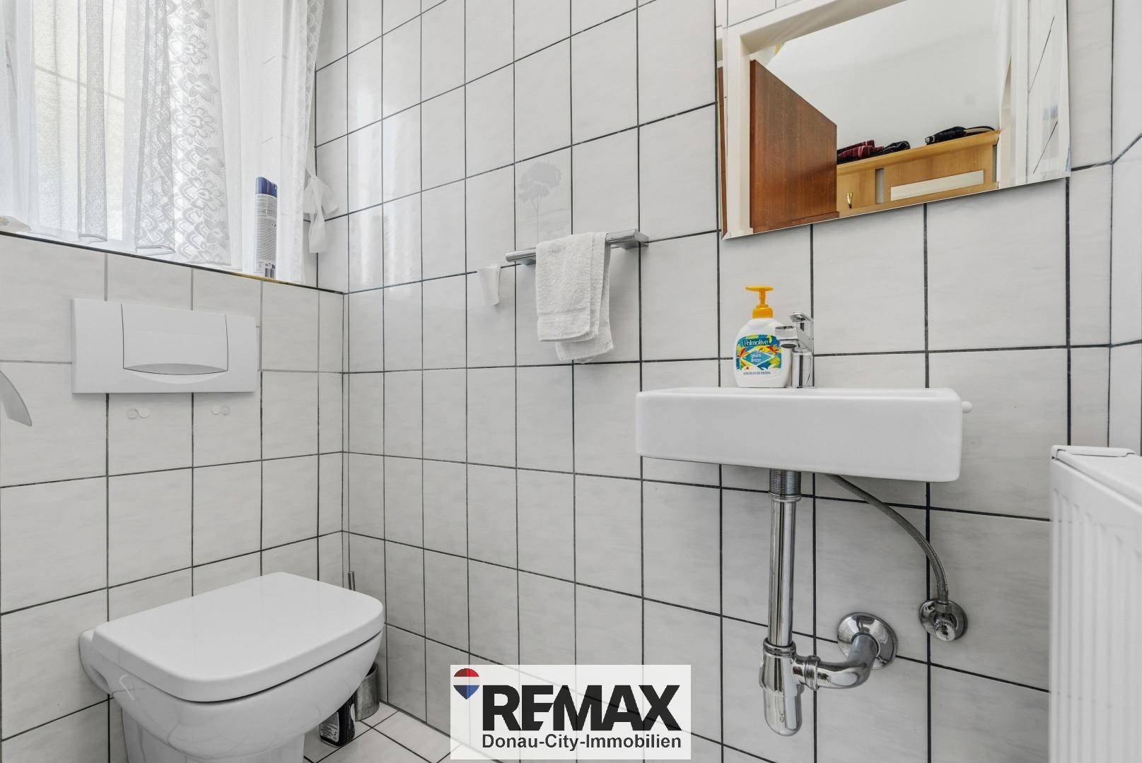 Kleines Gäste-WC mit weißen Fliesen, Waschbecken und Fenster.