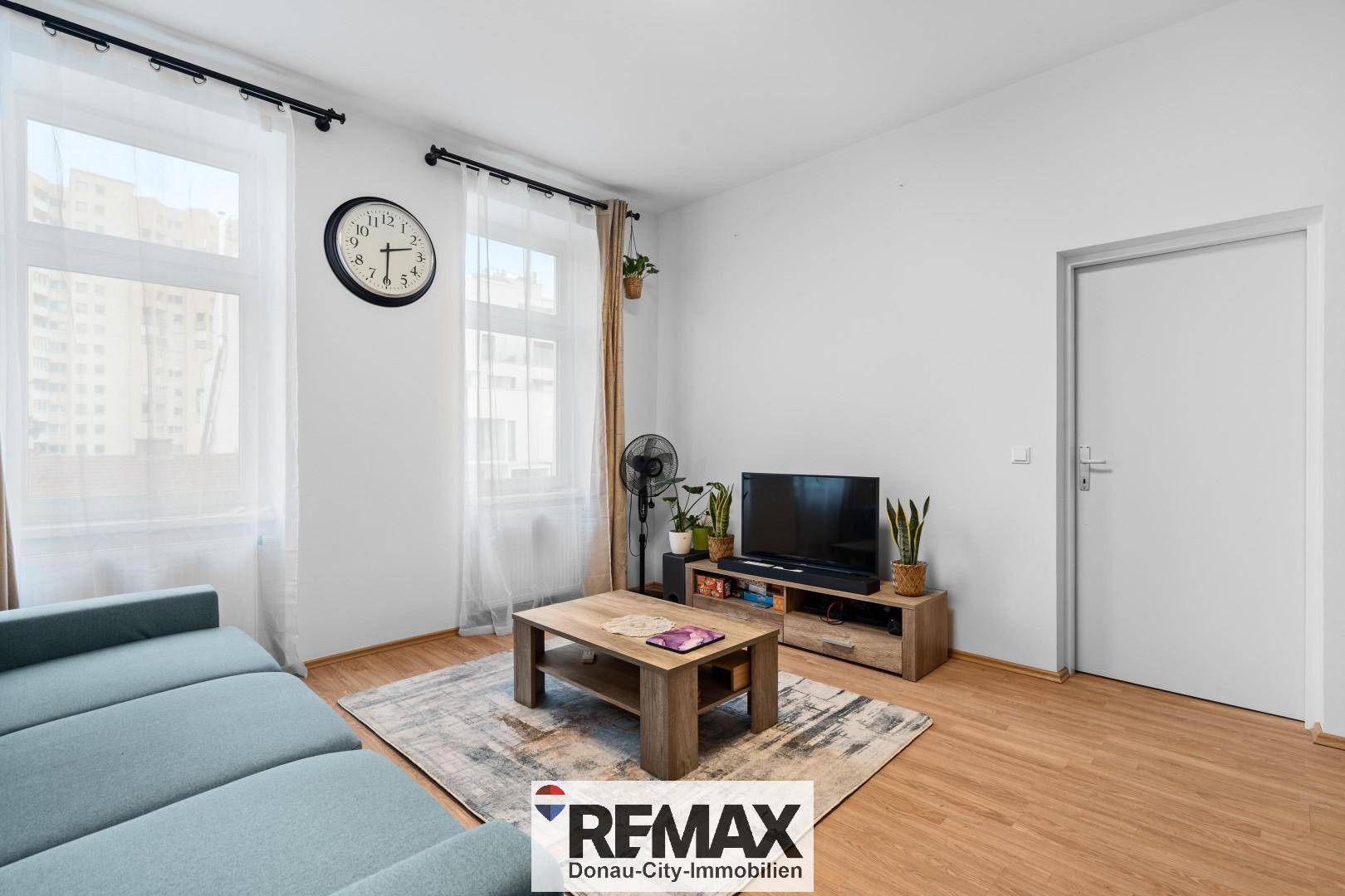 Wohnzimmer mit Laminatboden, Fernseher und Blick auf die Stadt durch große Fenster.