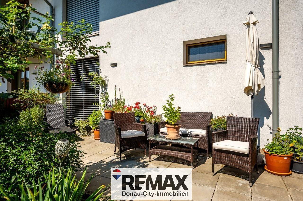 Gemütliche Terrasse mit Rattanmöbeln und Sonnenschirm, umgeben von Pflanzen.