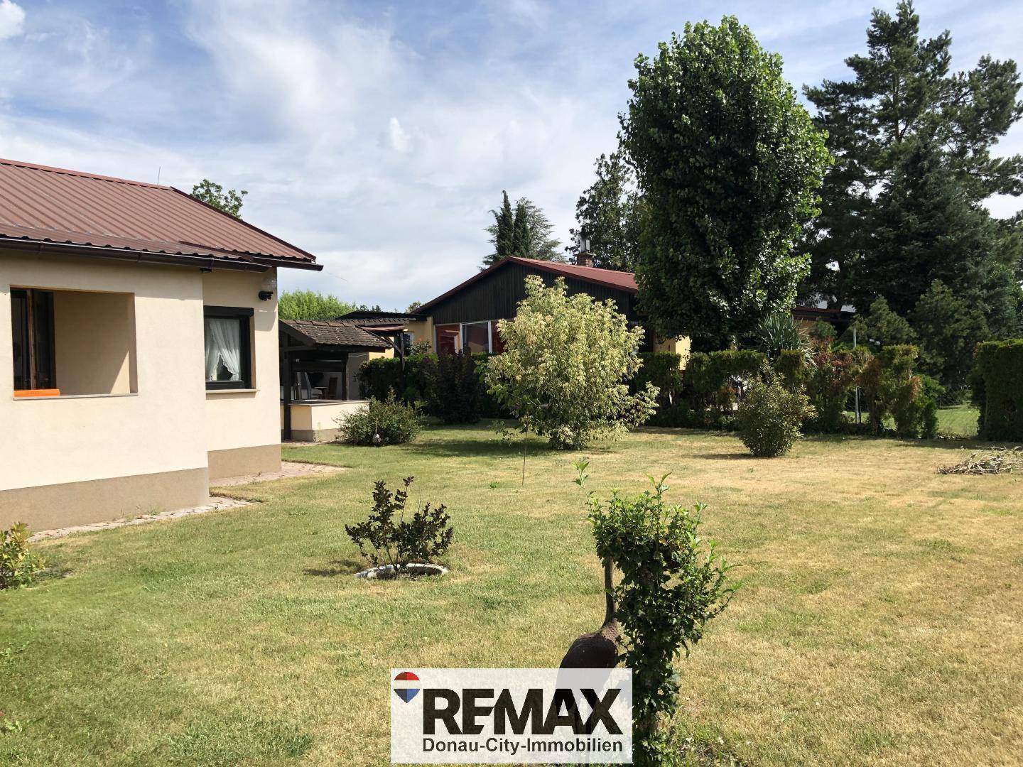 Weitläufiger Gartenbereich neben dem Haus mit großen Bäumen und Rasenfläche.