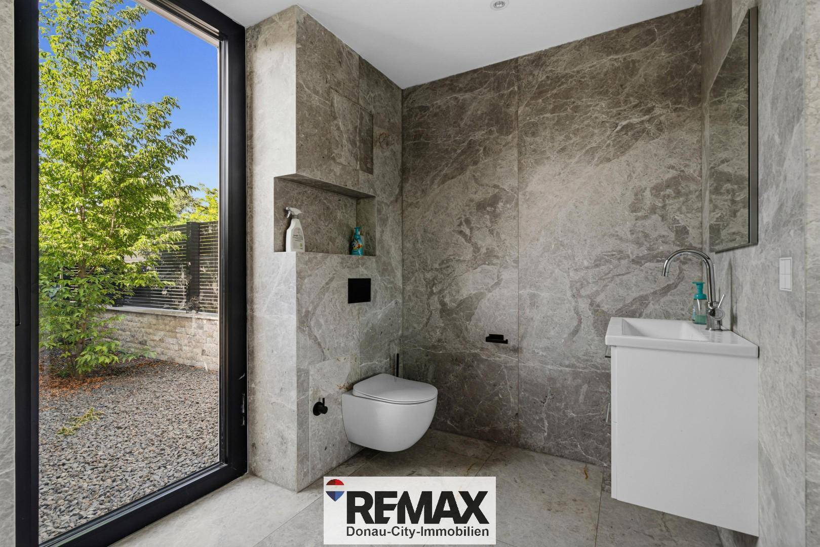 Modernes Gäste-WC mit Marmorfliesen, wandhängender Toilette und Fenster zum Garten.