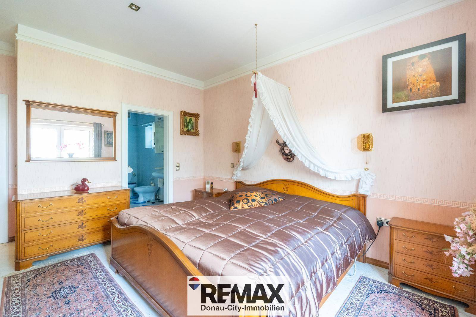 Schlafzimmer mit großem Bett, rosa Wänden und direktem Zugang zum Badezimmer.