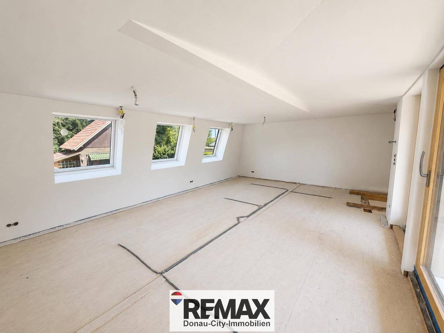 Geräumiger Obergeschossraum im Rohbau mit schrägen Decken und mehreren Dachfenstern für viel Licht.