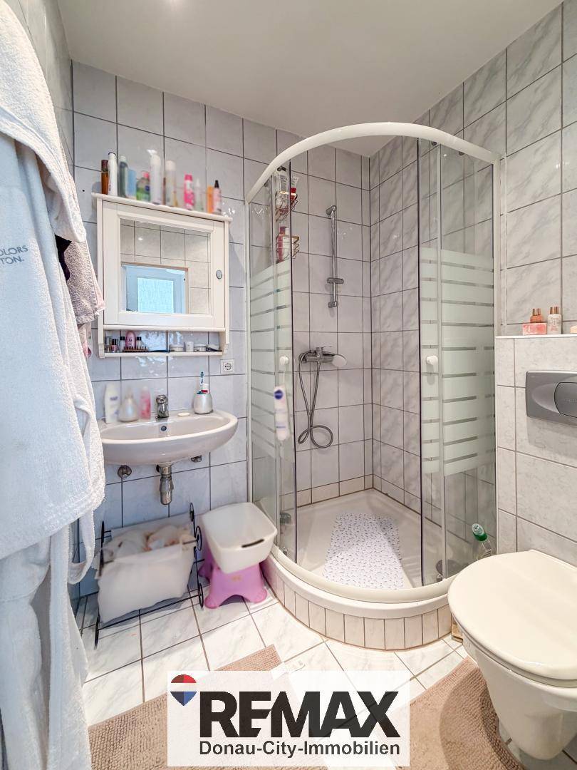 Gefliestes Badezimmer mit Duschkabine, Waschbecken und Toilette in hellem Design.