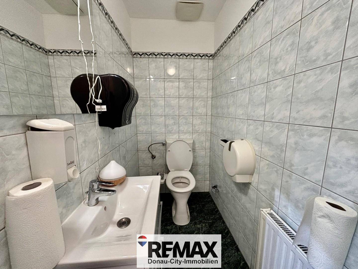 Kleiner Toilettenraum mit WC, Waschbecken und hellen Fliesen an den Wänden.