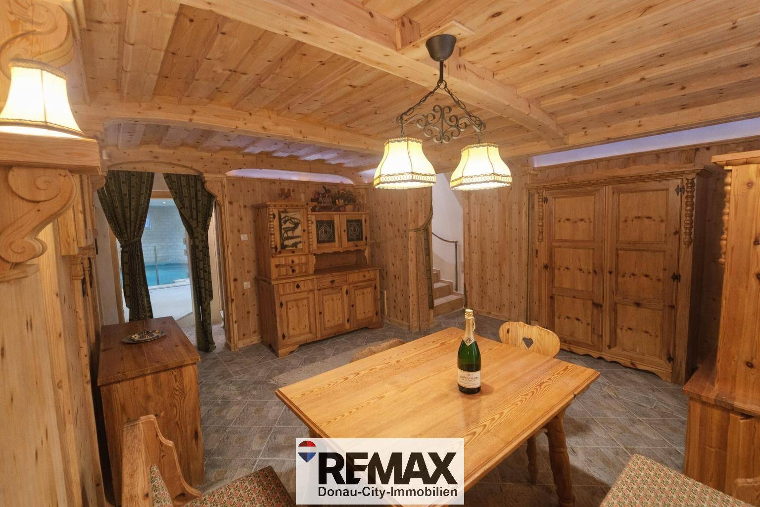 Rustikaler Essbereich mit Holzmöbeln, Holzvertäfelung und Blick auf den angrenzenden Poolbereich.