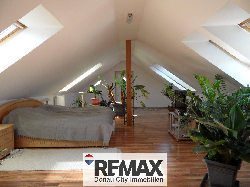 Helles Schlafzimmer im Dachgeschoss mit schrägen Wänden, Dachfenstern und Holzboden.