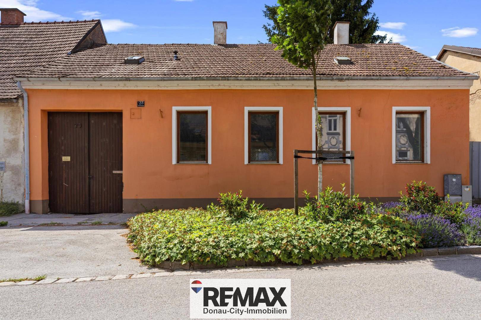 Vorderansicht eines Einfamilienhauses mit oranger Fassade, braunem Garagentor und kleinem Vorgarten.
