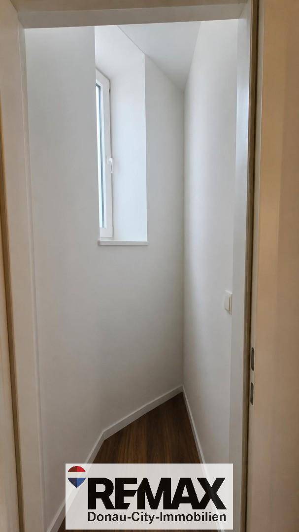 Schmaler Flur mit Fenster, der zu einem weiteren Bereich der Wohnung führt und Tageslicht spendet.
