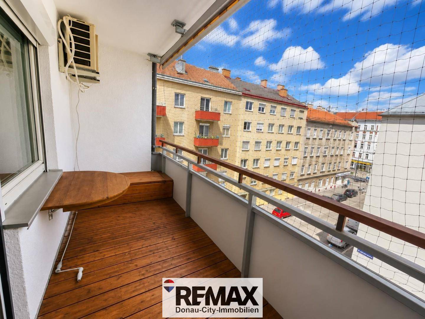 Kleiner Balkon mit Holzboden und Klapptisch, bietet einen Blick auf die umliegenden Gebäude.