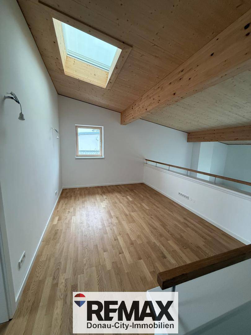Heller Wohnbereich mit Holzbalkendecke, Parkettboden und Dachfenster für viel Tageslicht.